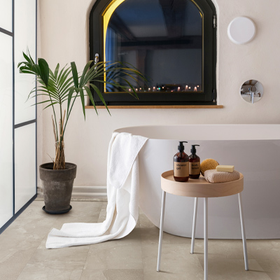 stone look luxury vinyl tile flooring in bathroom with plant and bathtub.